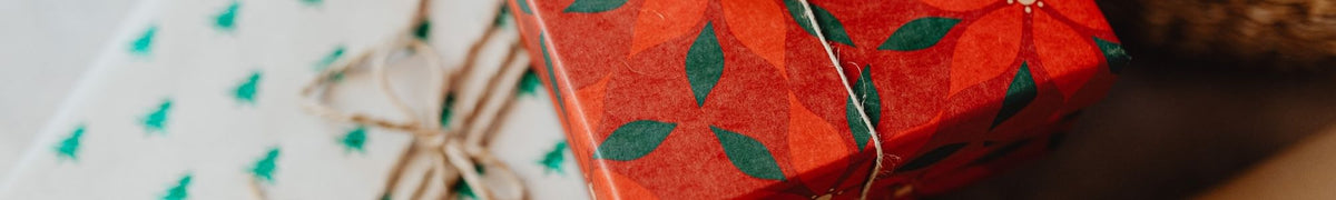 Cadeaux emballés dans du papier à motifs de sapins et de fleurs rouges, noués avec de la ficelle